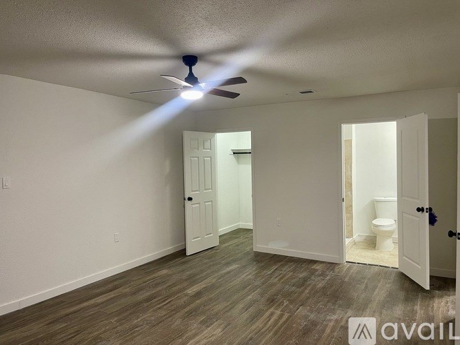 A room with a ceiling fan and a toilet in the background.