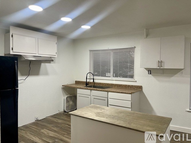 A kitchen with a black fridge, white cabinets, and a granite countertop.