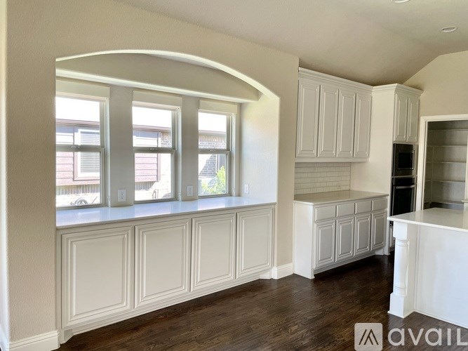 A kitchen with white cabinets and a window with a view of a street.
