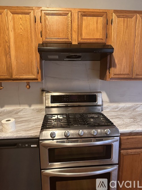 A stove with a black grill and a silver oven is in a kitchen with wooden cabinets.