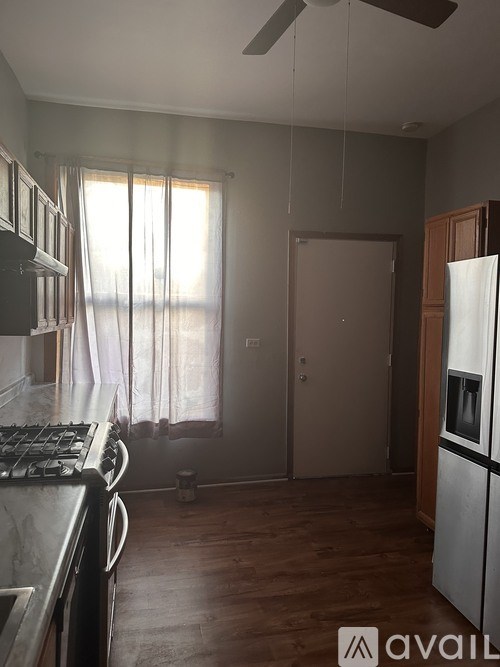 A kitchen with a stove, refrigerator, and a window with curtains.