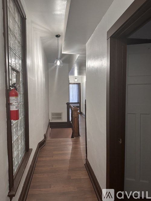 A hallway with a red fire extinguisher on the left and a door on the right.