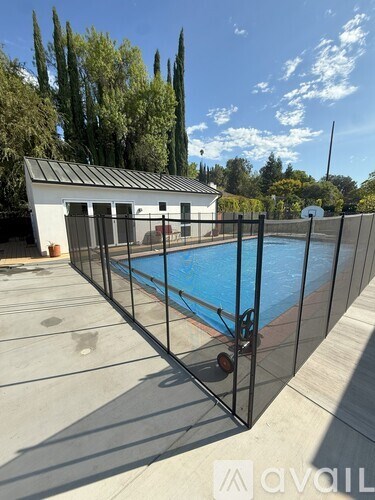 A pool surrounded by a black fence with a house in the background.