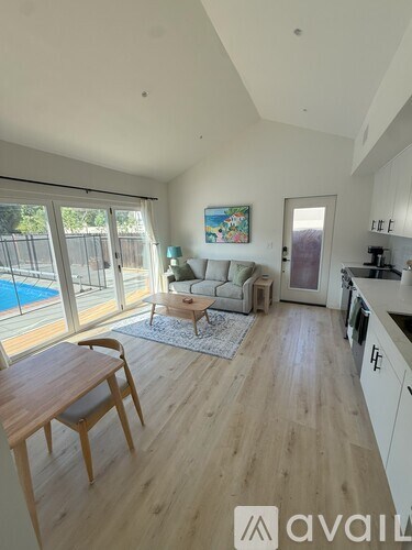 A living room with a wooden floor and a pool outside the window.