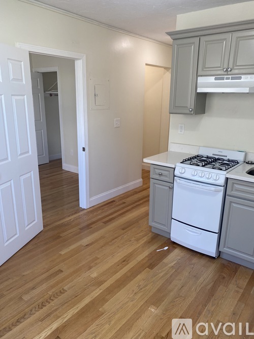 A kitchen with a white stove top oven and wooden floors.