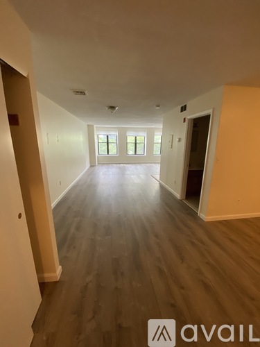 A long hallway with wood floors and a window with a view of trees.