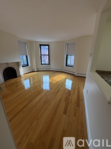 A room with wooden flooring and three windows.