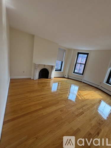 A room with wooden flooring and a fireplace with a window on the right side.