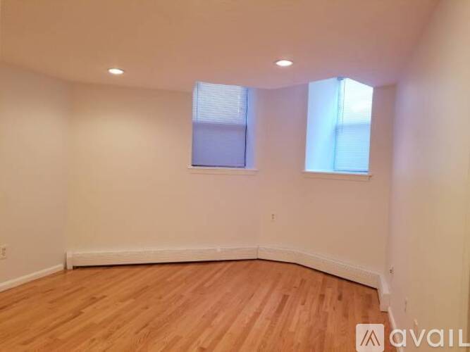 A room with wooden flooring and two windows.