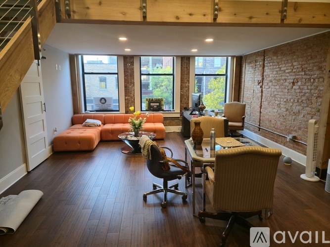 A room with wooden flooring and a staircase in the background.