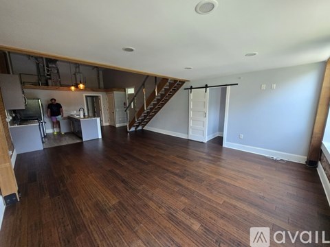 A room with wooden flooring and a staircase in the background.