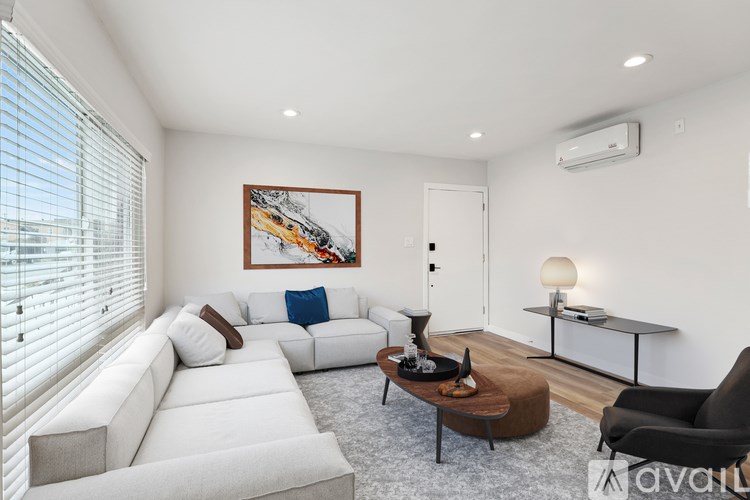 A living room with a white couch, a brown ottoman, and a painting on the wall.