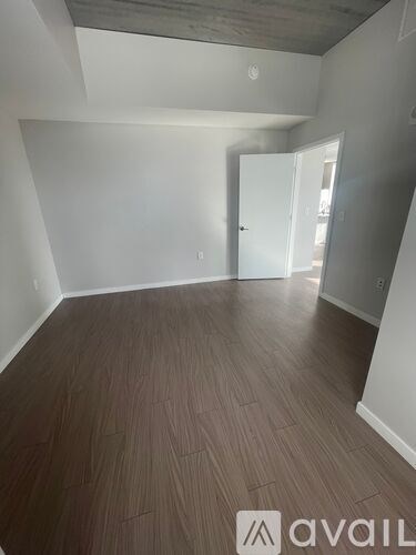 A room with wooden flooring and white walls, with a doorway leading to another room.