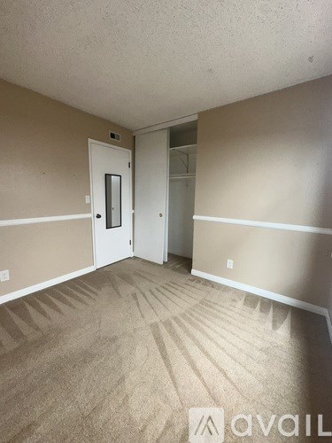 A room with beige carpet and walls, a white door, and a window.