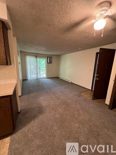 A carpeted room with a door on the right and a window with blinds on the left.