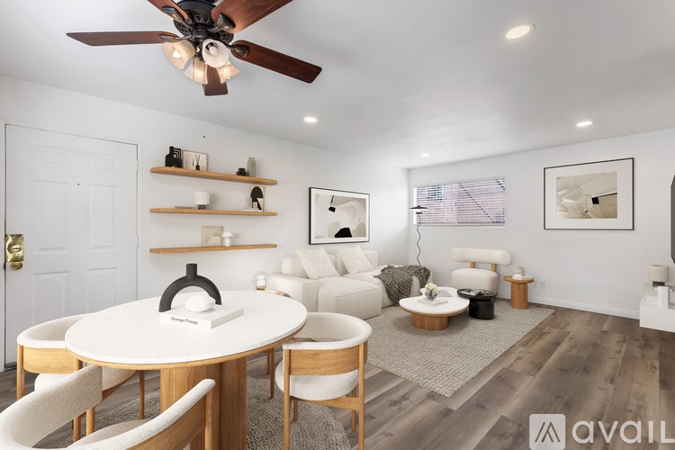 A modern dining room with a white table and chairs, a ceiling fan, and a couch in the background.