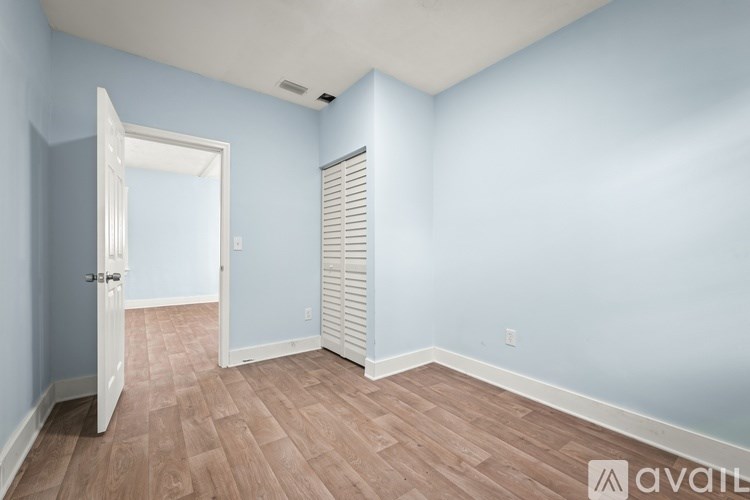 A room with light blue walls and wooden flooring with a white door.