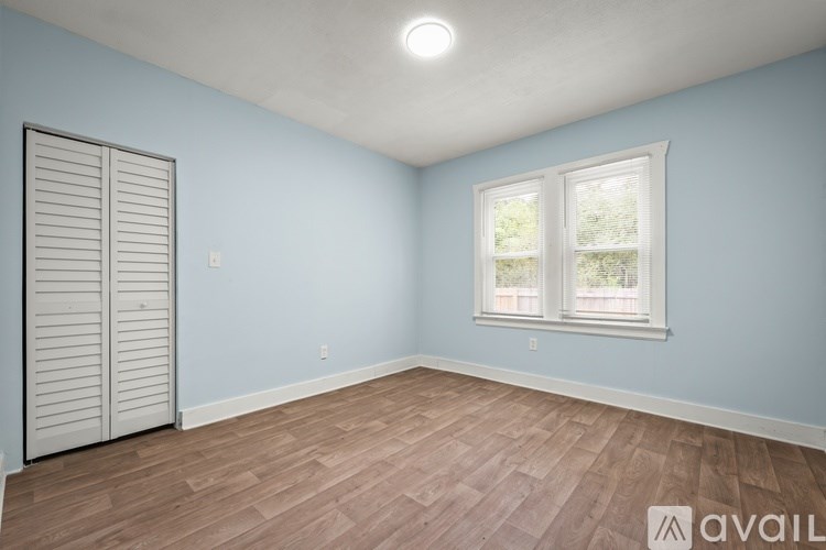 A room with light blue walls, a window with white trim, and a wooden floor.