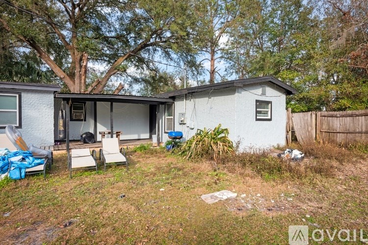 A small house with a white exterior is surrounded by trees and has a blue object on the ground.