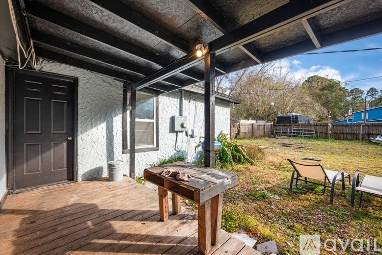 A wooden table is on a deck with a house in the background.