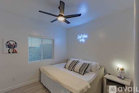 A bedroom with a bed, a ceiling fan, and a nightstand with a lamp.