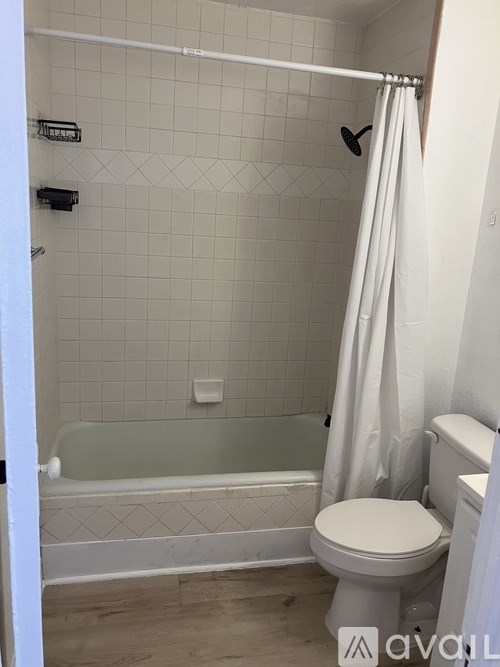 A white toilet sits in a bathroom with a white shower curtain.