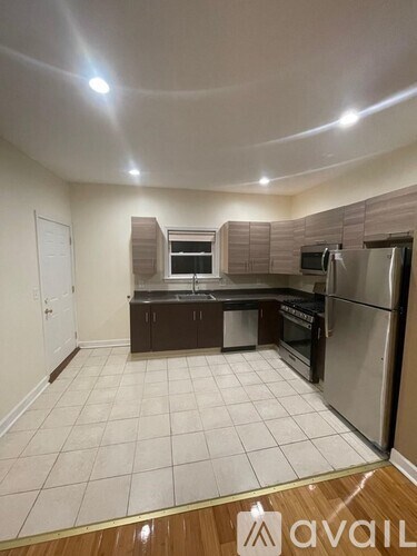 A kitchen with white tiles on the floor and a wooden floor in the foreground.