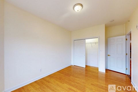 A room with wooden floors and a white wall with a doorway leading to another room.
