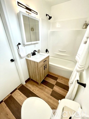 A white toilet is in a bathroom with wood flooring and a white tub.