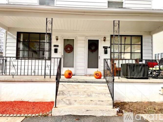 A white house with a black iron fence and two carved pumpkins on the steps.