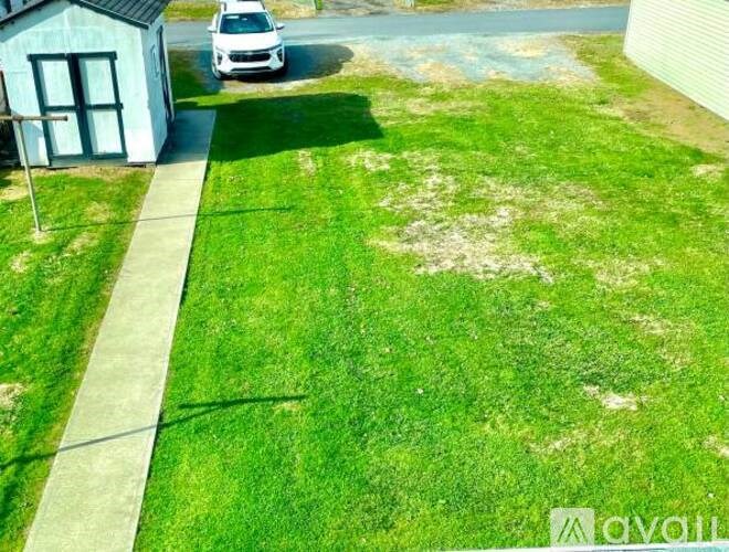A white car is parked in a driveway next to a small house.