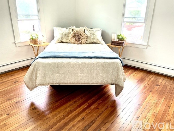A bed with a blue blanket and a pillow is in the middle of a room with wooden floors.
