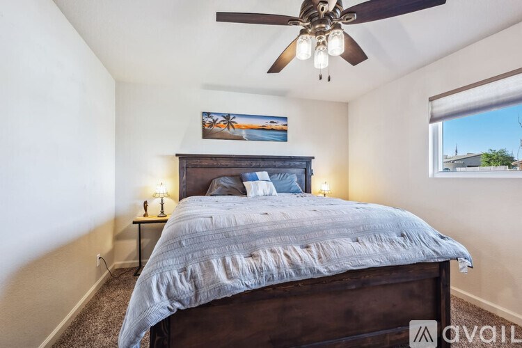 A bedroom with a bed, a ceiling fan, and a painting on the wall.