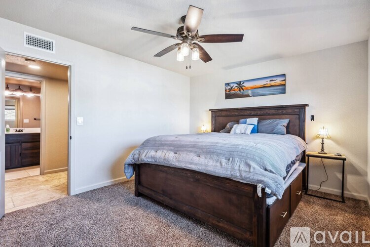 A bedroom with a bed, ceiling fan, and a painting on the wall.