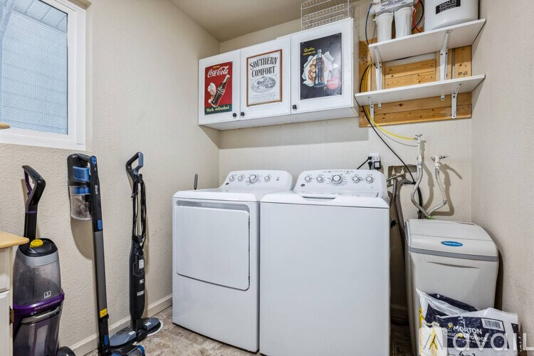 A small laundry room with a washer and dryer, a vacuum cleaner, a mop, and a broom.