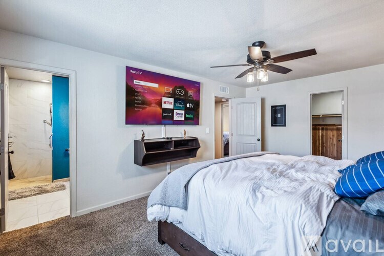 A bedroom with a bed, a ceiling fan, and a TV mounted on the wall.