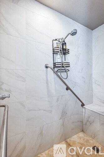 A shower with a marble wall and a metal grab bar.