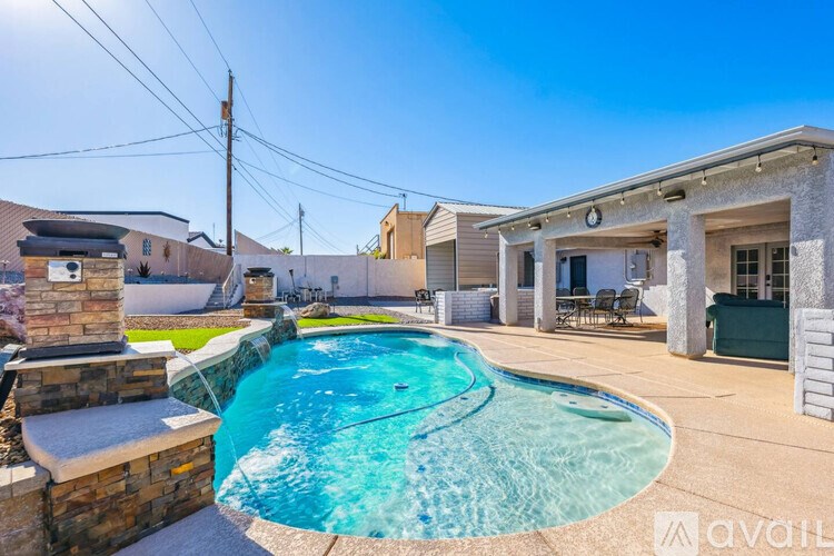 A swimming pool in a backyard with a stone pillar and a house in the background.