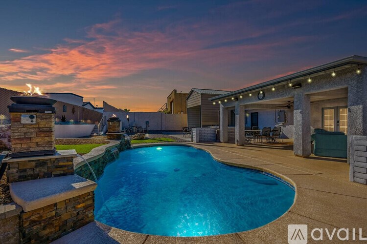 A pool surrounded by a stone wall and a house with lights on it.