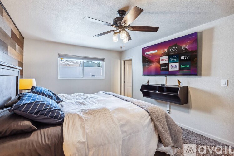 A bedroom with a bed, a ceiling fan, and a wall-mounted TV displaying various streaming services.