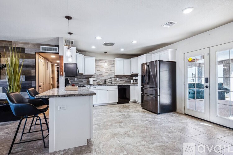 A modern kitchen with a white island and black chairs.