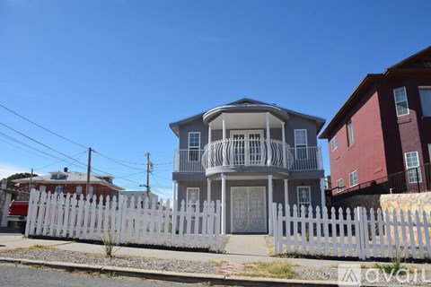 A white picket fence surrounds a two-story house with a balcony.
