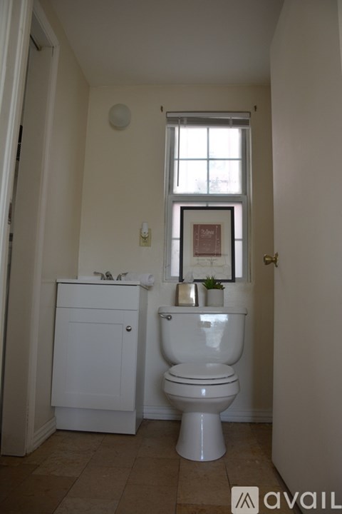 A white toilet in a bathroom with a window above it.