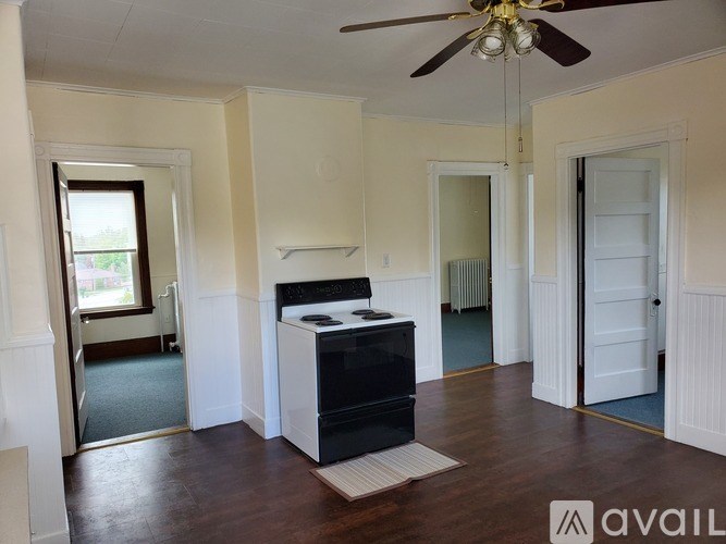 A room with a black and white fridge, a ceiling fan, and a window.