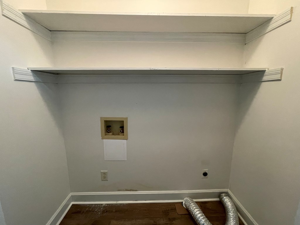 A white wall with a shelf and a pipe on the floor.