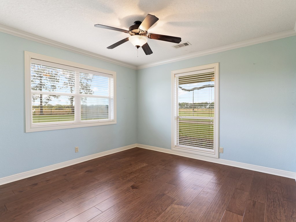 A room with a ceiling fan and two windows.