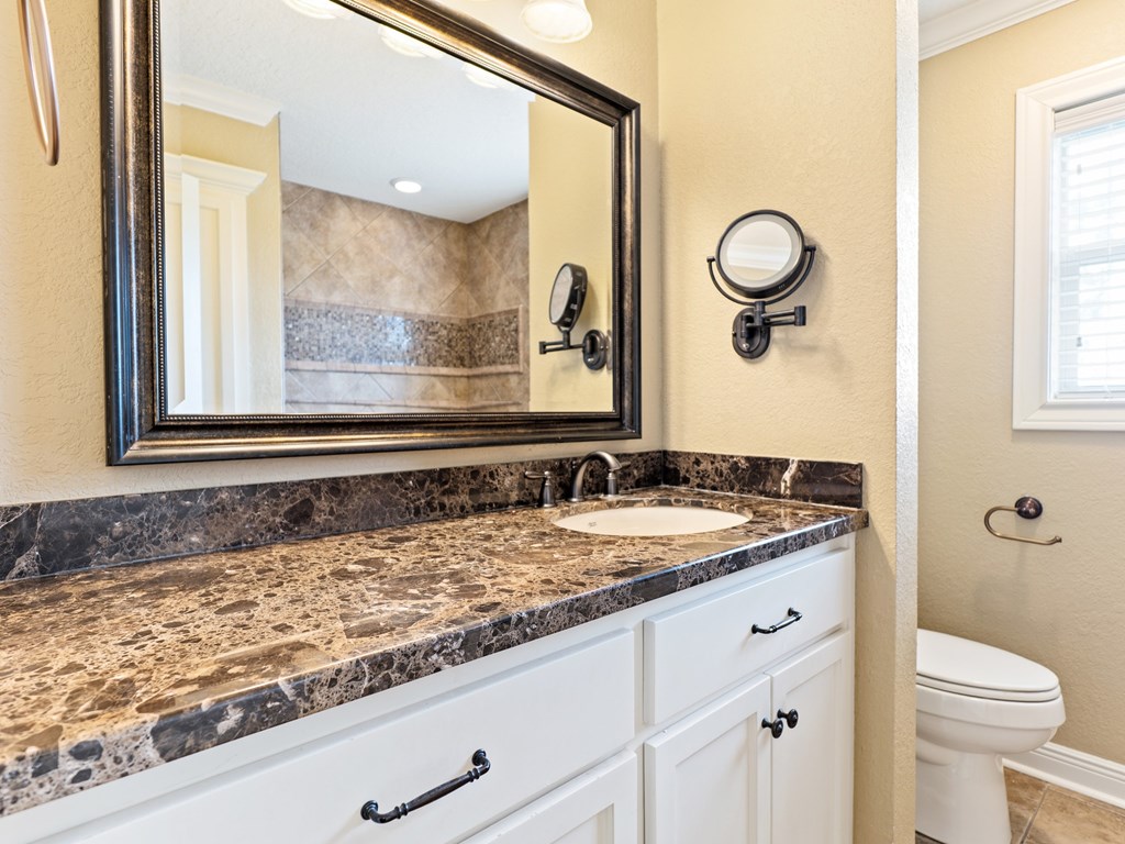 A bathroom with a marble countertop and white cabinets.