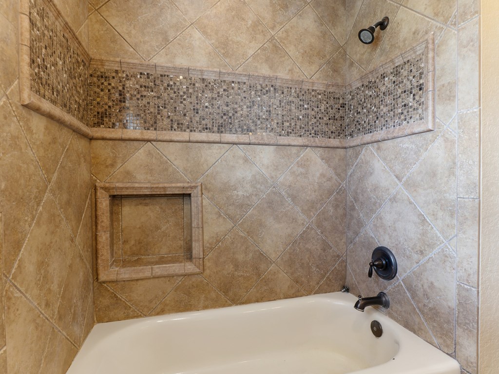 A bathroom with a tiled shower and a white bathtub.