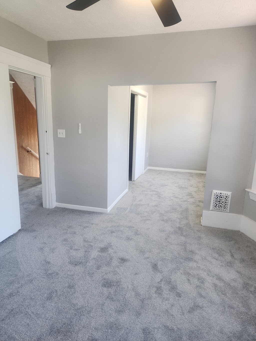 A room with a carpeted floor and a ceiling fan.