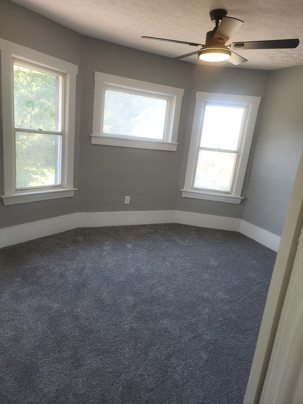 A room with a ceiling fan and three windows.